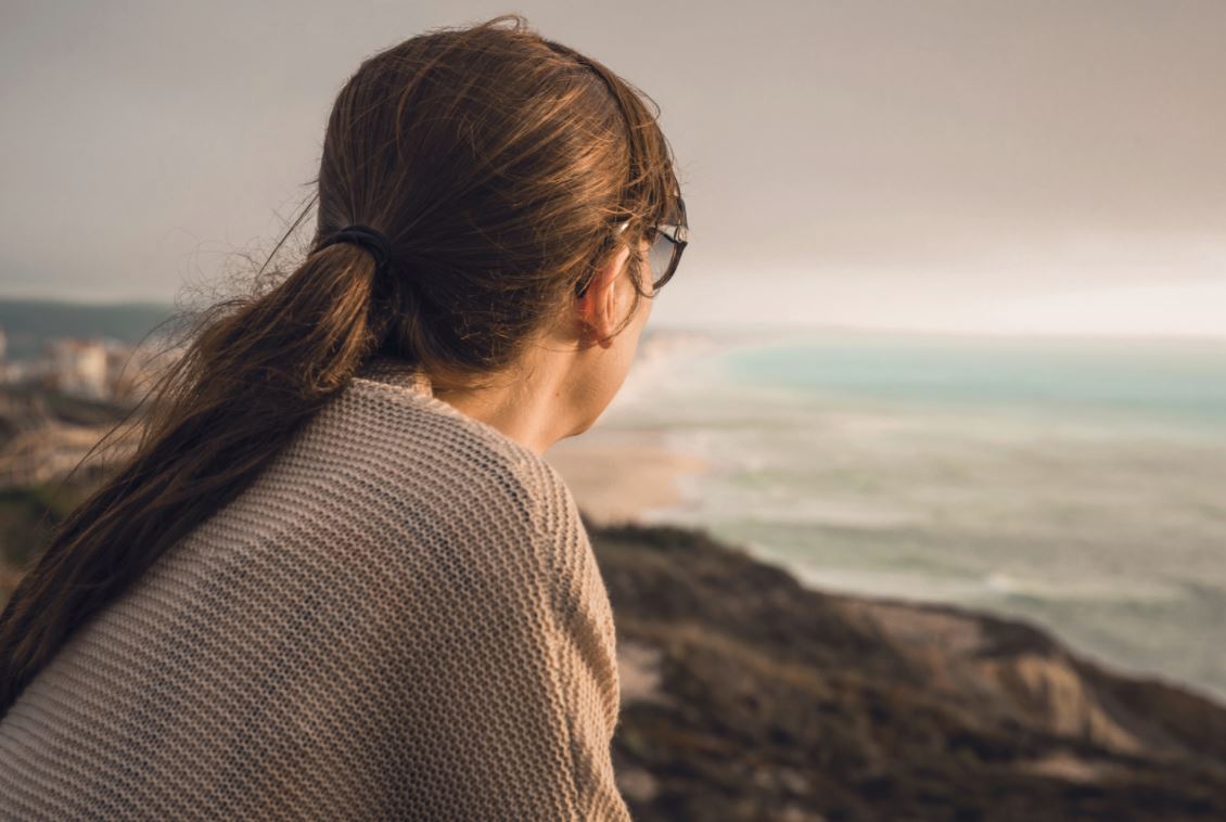 Person in a grey knit sweater looking out over the sea.